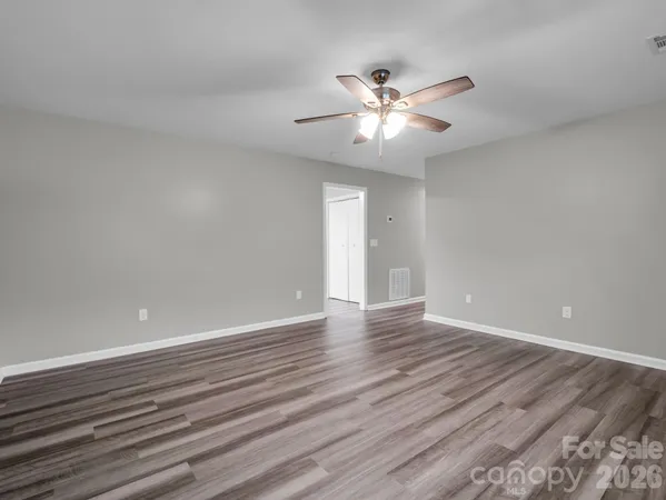a view of an empty room with wooden floor and a ceiling fan