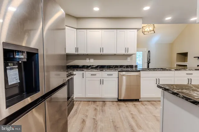 a large white kitchen with granite countertop a stove top oven a sink a counter space and cabinets