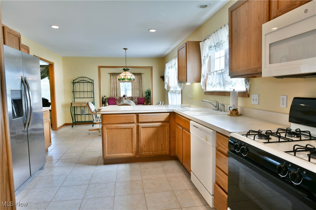 1997 East County Line Road Mineral Ridge, OH 44440 - Photo 13 of 35 Kitchen featuring hanging light fixtures, kitchen peninsula, white appliances, sink, and light tile patterned floors