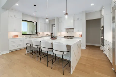 a kitchen with kitchen island a dining table chairs sink and white cabinets