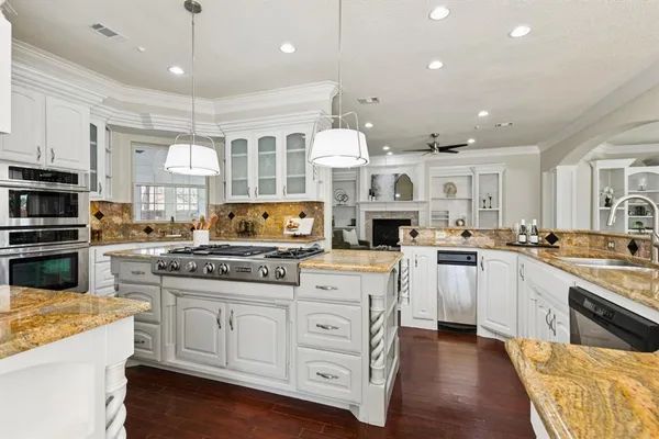 a kitchen with stainless steel appliances granite countertop a stove top oven a sink dishwasher and a refrigerator with wooden floor