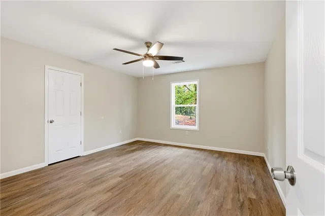 an empty room with wooden floor ceiling fan and windows