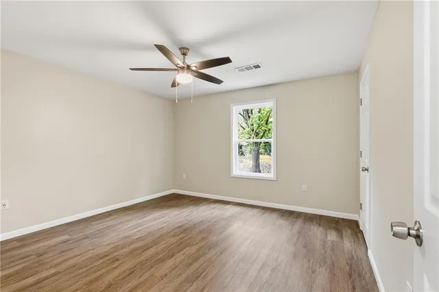 an empty room with wooden floor fan and windows