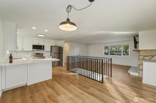 a open kitchen with kitchen island a stove a sink a refrigerator and white cabinets with wooden floor