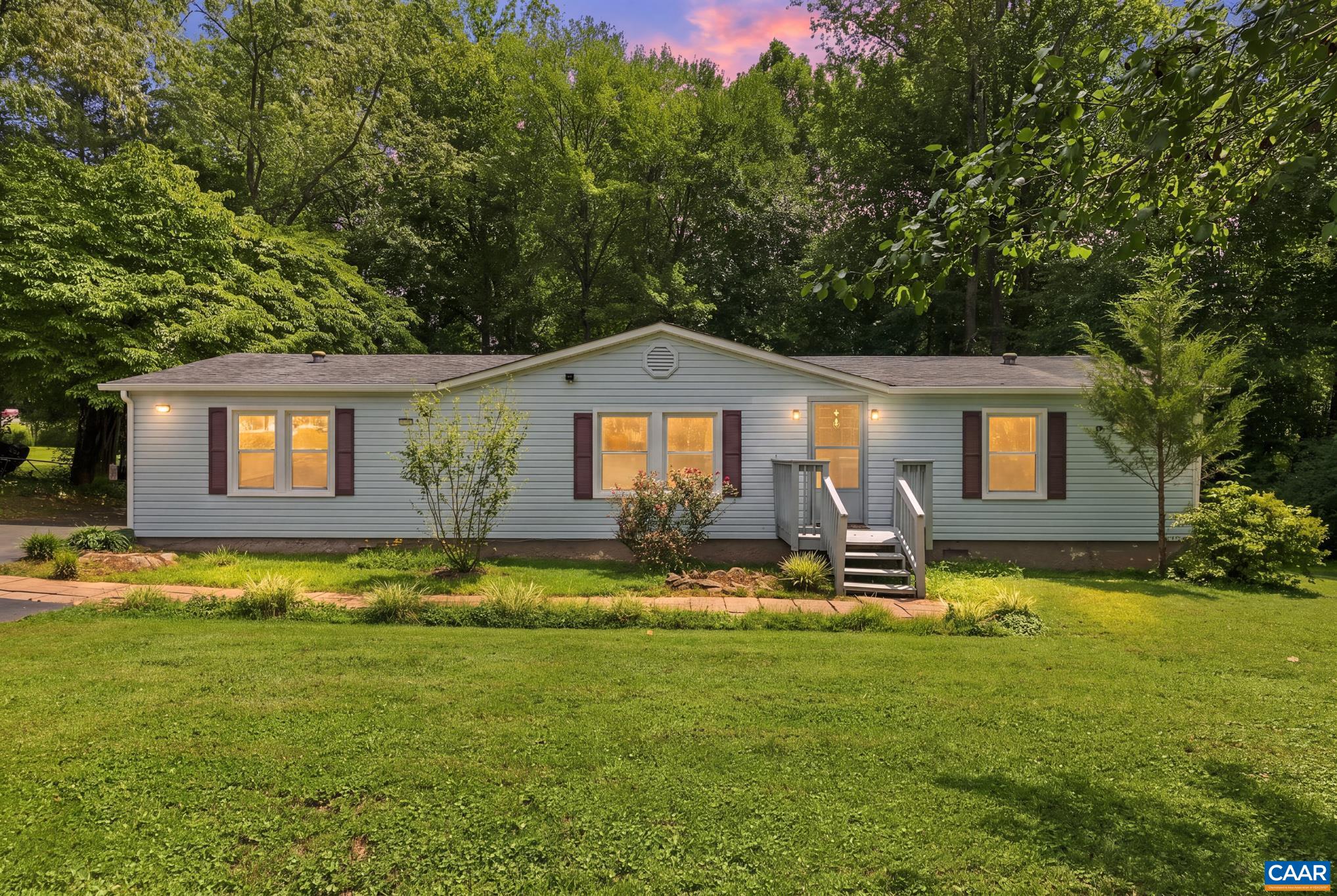 61 Snapdragon Road Ruckersville, VA 22968 - Photo 35 of 47 Lovely single-story home framed by mature trees and a vibrant lawn! Features warm exterior lighting, charming dark shutters, a covered entry porch, and dusk-lit windows that create an irresistible, move-in-ready welcome.