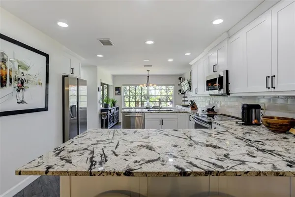 a kitchen with stainless steel appliances granite countertop a refrigerator a stove a sink a microwave a refrigerator and white cabinets with wooden floor