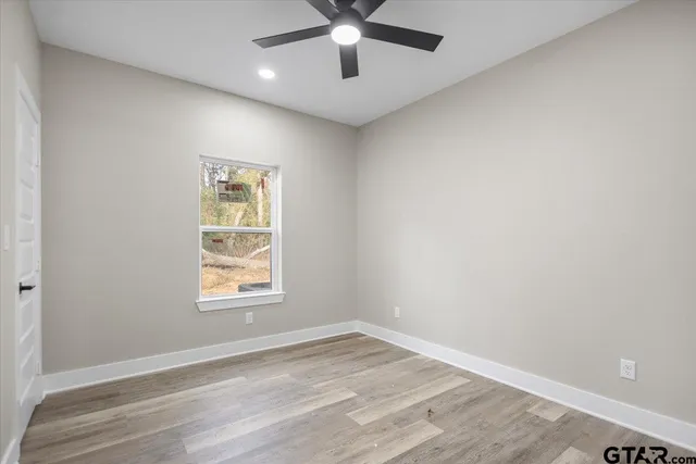 an empty room with wooden floor chandelier fan and windows