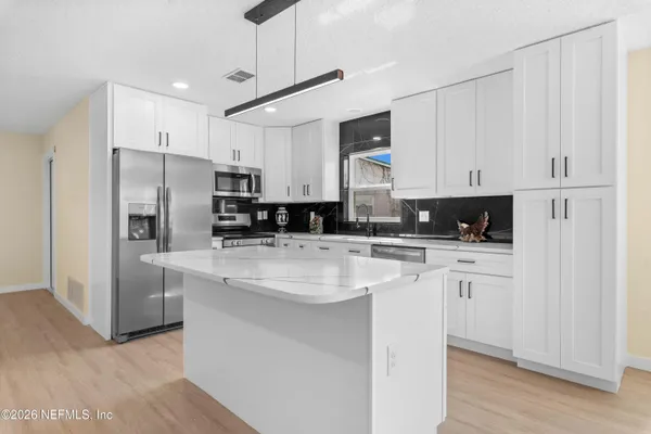 a kitchen with stainless steel appliances granite countertop a refrigerator a stove a sink and white cabinets with wooden floor