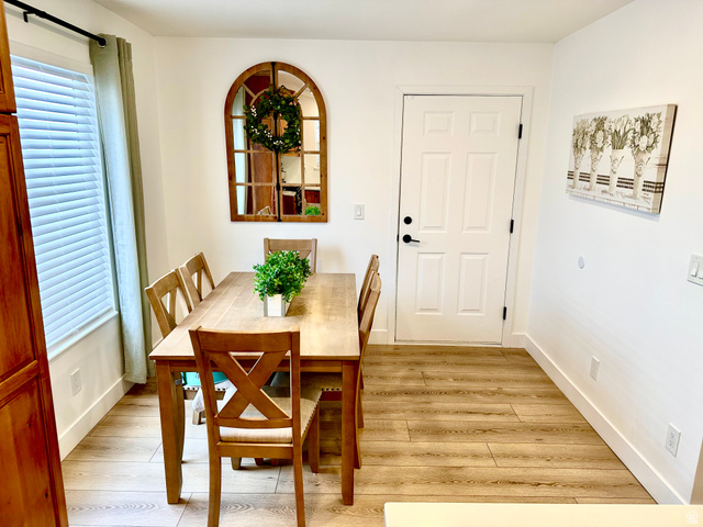 7818 North Windhover Road Eagle Mountain, UT 84005 - Photo 11 of 32 Dining area featuring wood-finish flooring, white baseboards, a white paneled door with black hardware, and a window with blinds