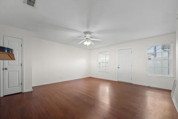 an empty room with wooden floor chandelier fan and windows