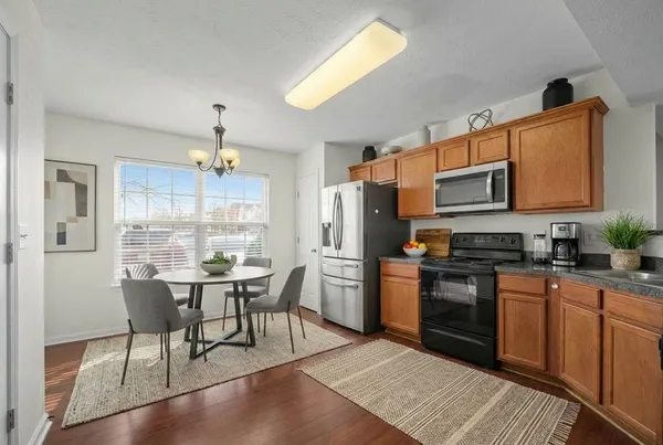 a kitchen with stainless steel appliances granite countertop a stove a sink dishwasher a refrigerator and a dining table with wooden cabinet