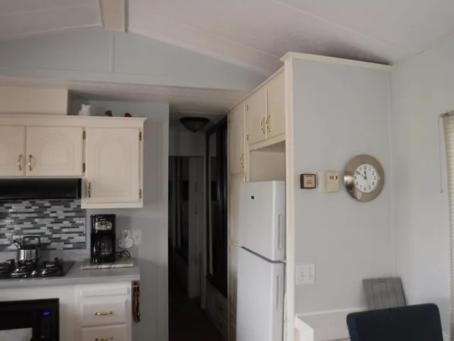 a kitchen with a refrigerator a stove top oven a clock and white cabinets