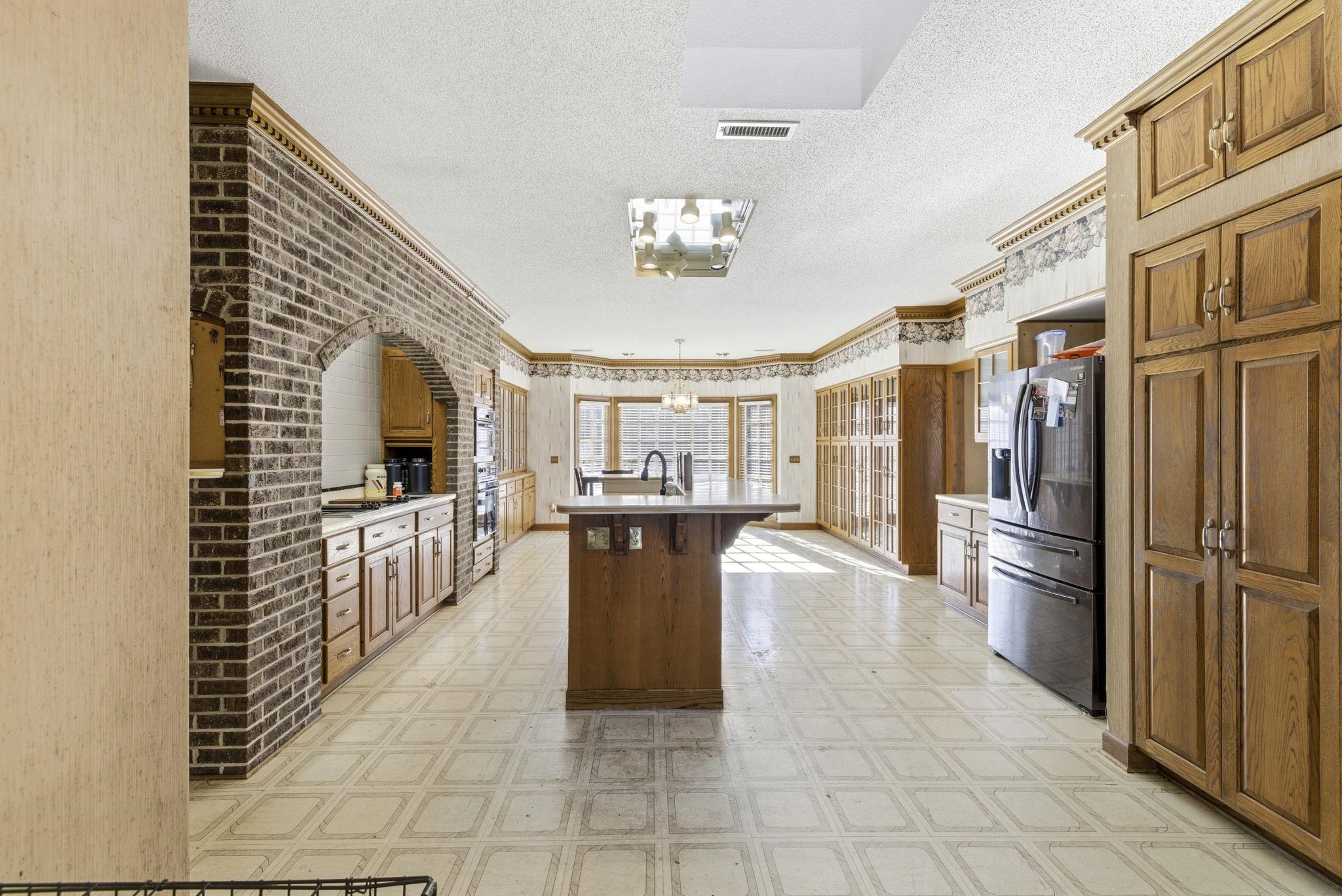 485 Carolina Drive Loris, SC 29569 - Photo 10 of 40 Kitchen featuring brown cabinetry, a center island with sink, crown molding, stainless steel fridge with ice dispenser, and a chandelier