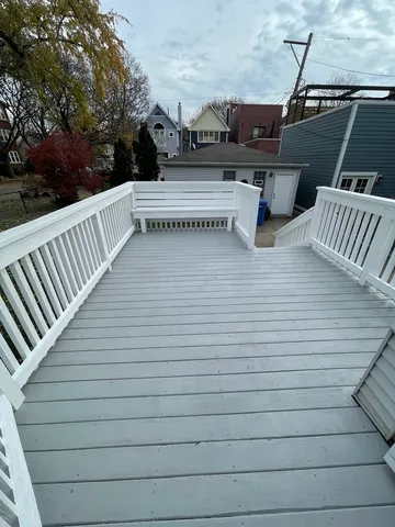 a view of a white house in front of a big yard with plants and large trees