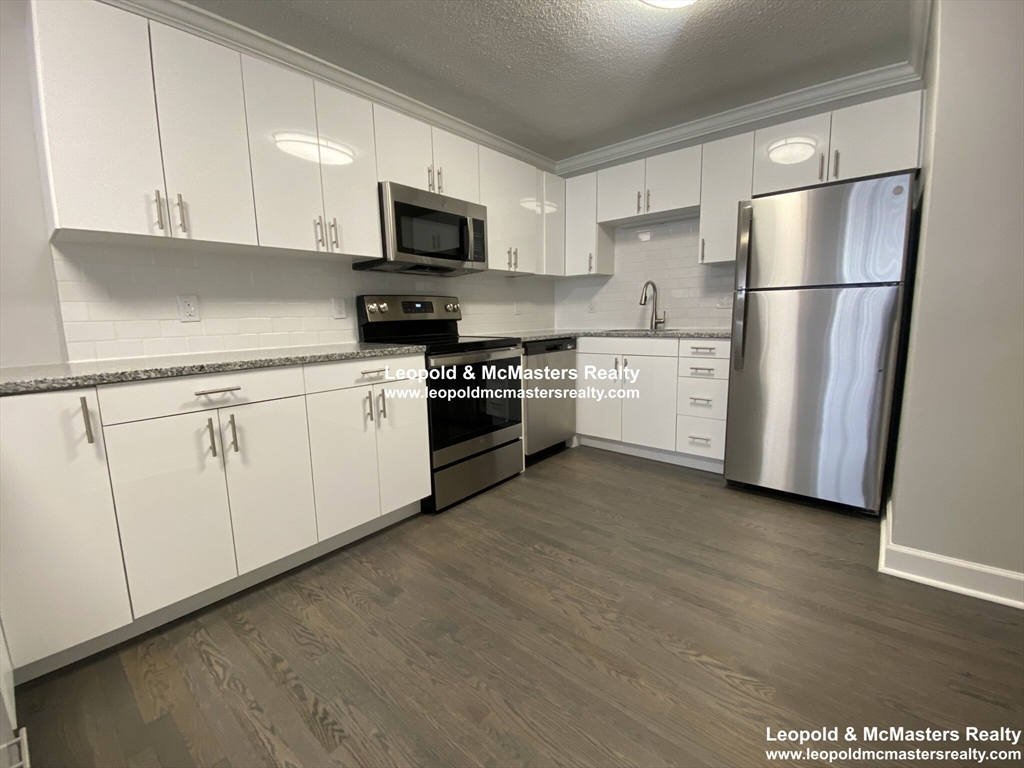 519 Washington Street, Unit 2 Brookline, MA 02446 - Photo 2 of 11 a kitchen with white cabinets stainless steel appliances and a refrigerator