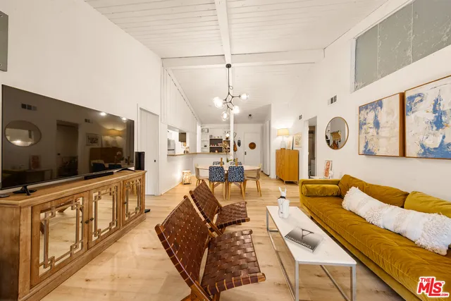 a view of a dining room and livingroom with furniture wooden floor a rug a flat screen tv a painting and a chandelier