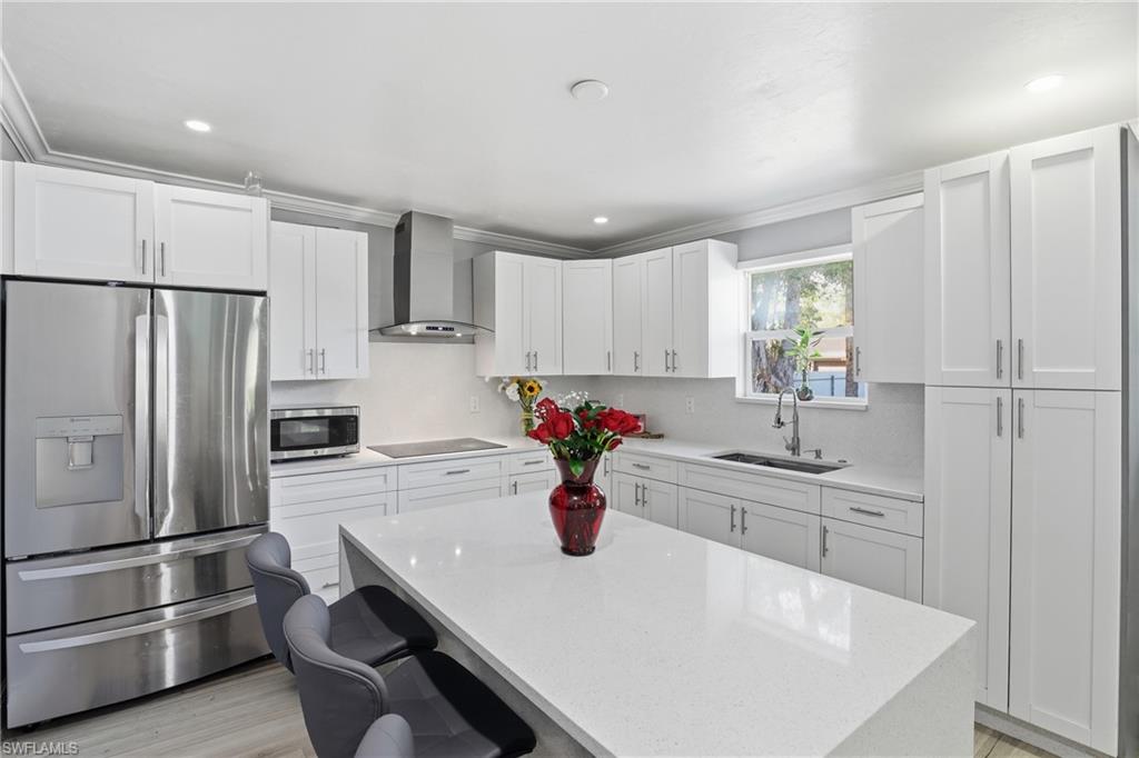 6005 Star Grass Lane Naples, FL 34116 - Photo 14 of 44 Kitchen featuring stainless steel appliances, light stone counters, white cabinets, light wood-style flooring, and a center island