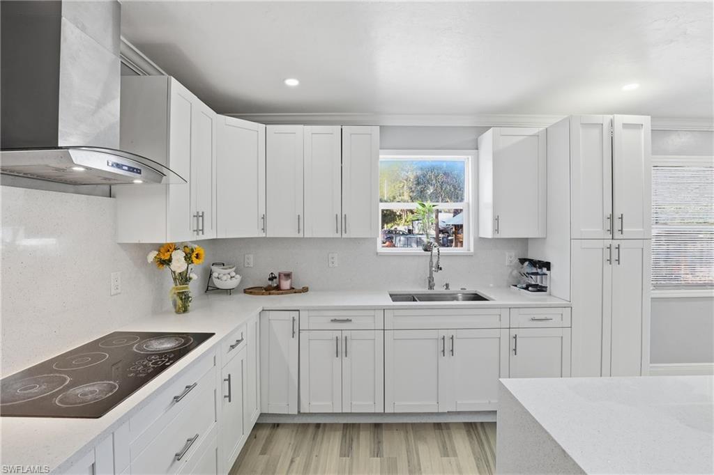 6005 Star Grass Lane Naples, FL 34116 - Photo 15 of 44 Kitchen featuring black electric cooktop, light stone countertops, light wood-type flooring, white cabinets, and decorative backsplash