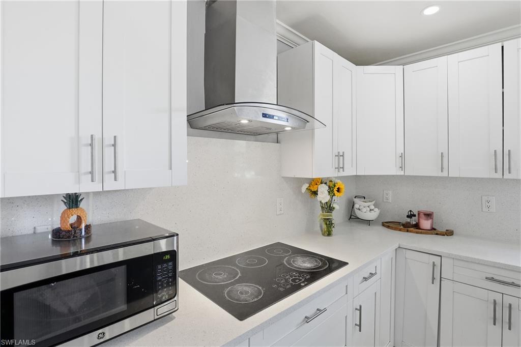6005 Star Grass Lane Naples, FL 34116 - Photo 16 of 44 Kitchen with stainless steel microwave, black electric stovetop, white cabinets, and light stone countertops