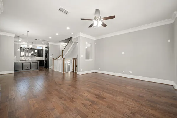 an empty room with wooden floor kitchen view and a ceiling fan