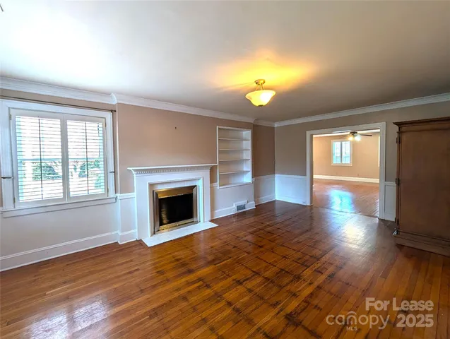 an empty room with wooden floor fireplace and windows