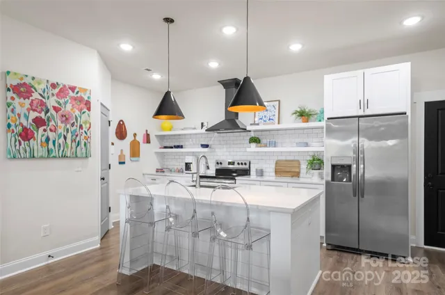 a kitchen with stainless steel appliances granite countertop a sink a stove a refrigerator and a dining table with wooden floor