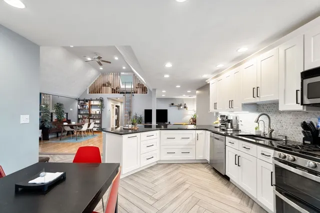 a kitchen with stainless steel appliances kitchen island granite countertop a sink dishwasher stove and white cabinets with wooden floor