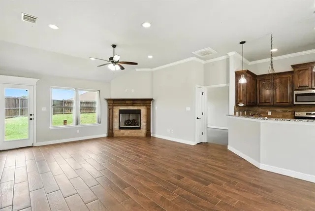 a view of an empty room with wooden floor and a kitchen
