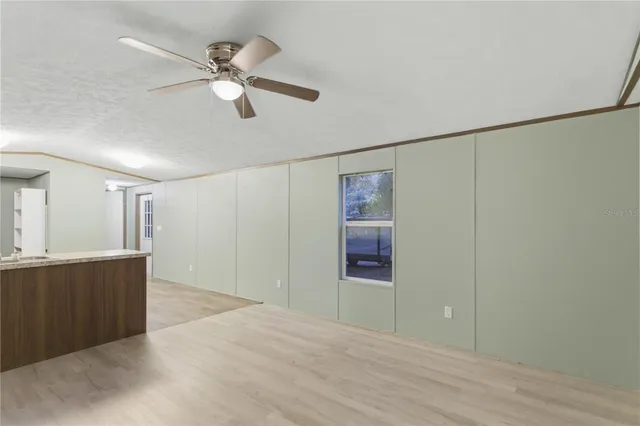 a view of an empty room with wooden floor and a ceiling fan