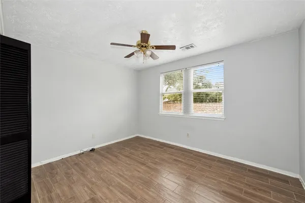 an empty room with wooden floor ceiling fan and windows