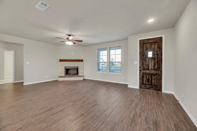 an empty room with wooden floor fireplace and windows