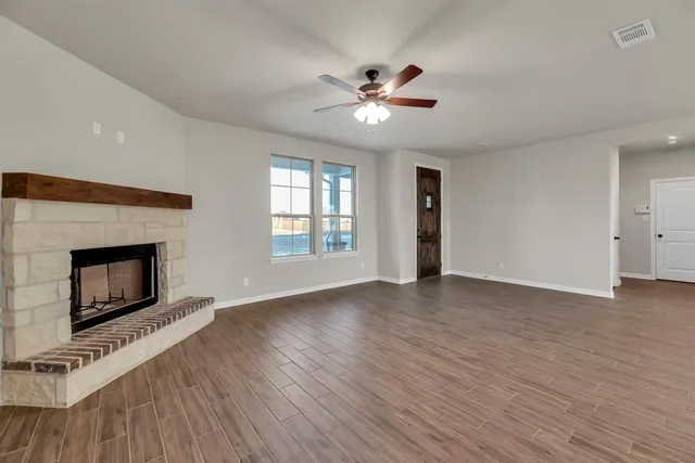 a view of an empty room with wooden floor fireplace and a window