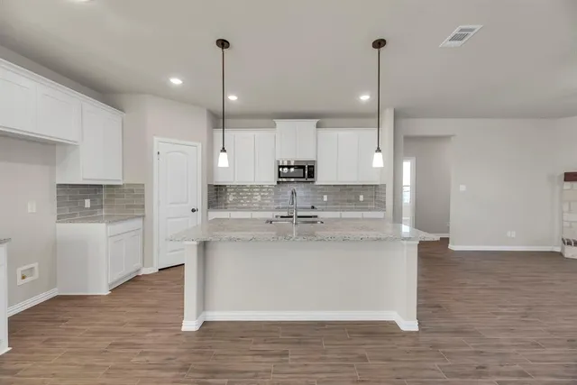 a large kitchen with stainless steel appliances granite countertop a sink a stove a refrigerator and white cabinets with wooden floor