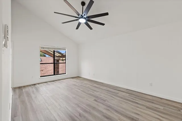 an empty room with wooden floor chandelier fan and windows
