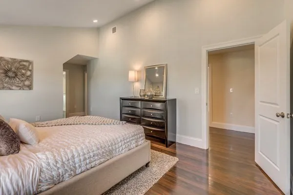 a bedroom with a bed and dresser with wooden floor