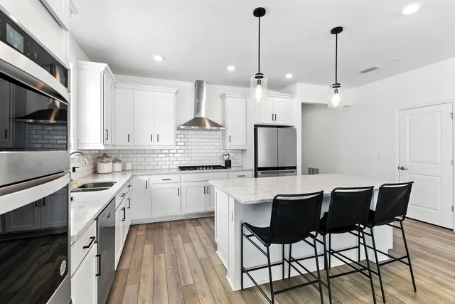 a kitchen with stainless steel appliances granite countertop a refrigerator a stove a oven a sink dishwasher and a dining table with wooden floor