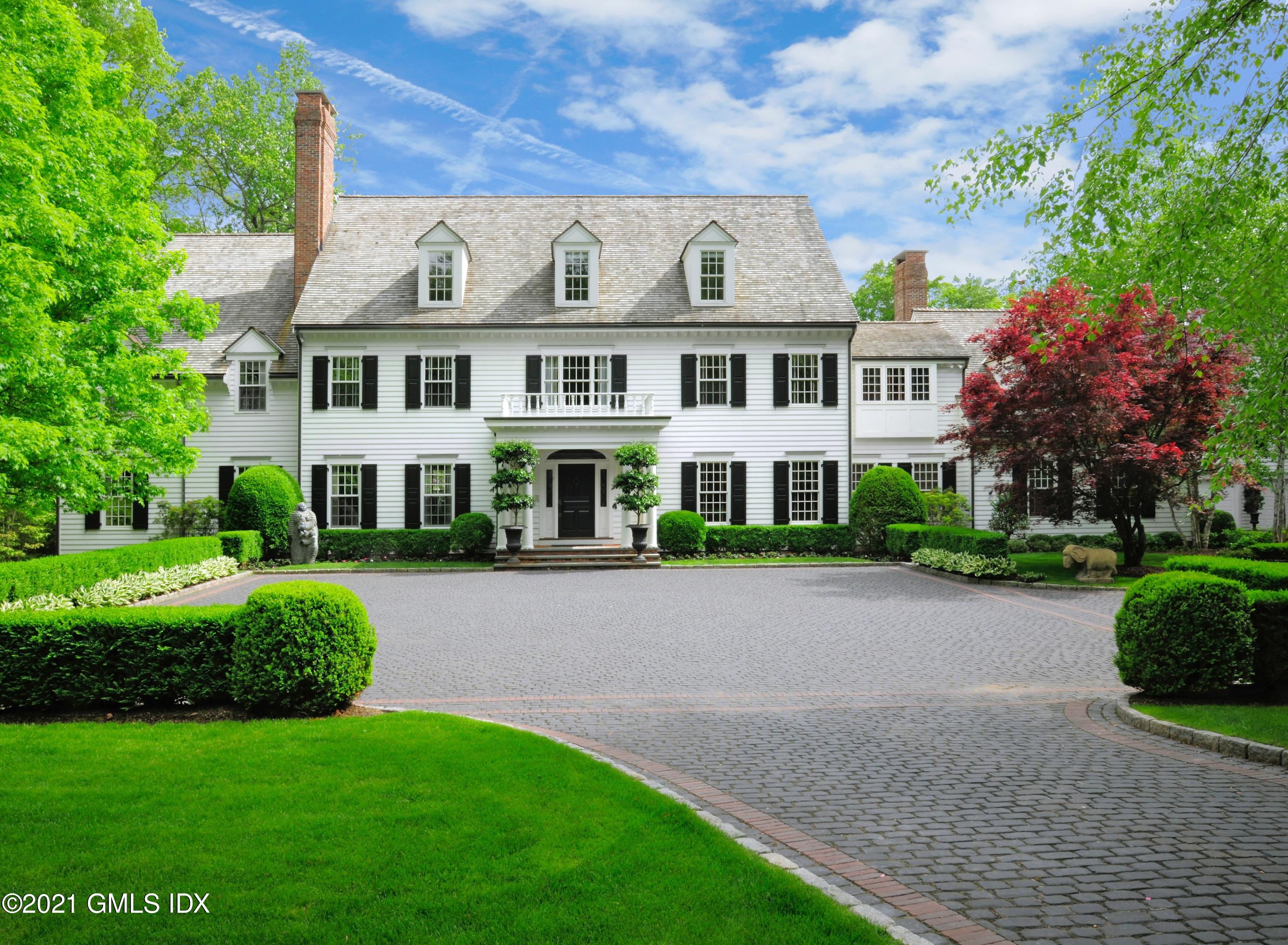 a view of a white house with a big yard plants and large trees