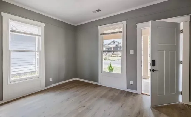 a view of an empty room with wooden floor and a window