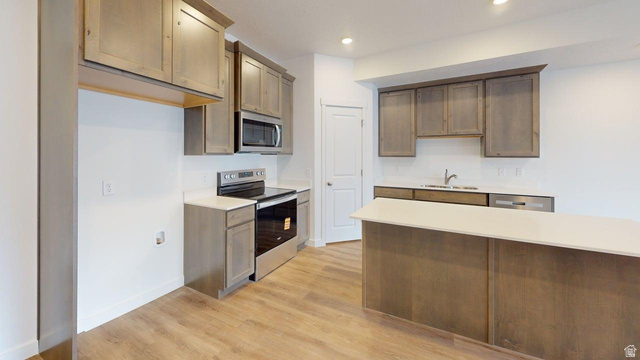 777 Pheasantbrook Drive, Unit 2B Centerville, UT 84014 - Photo 9 of 42 Contemporary kitchen featuring wood-finish flooring, light wood-tone cabinetry, stainless steel appliances, a white subway tile backsplash, and an island with a light-toned countertop