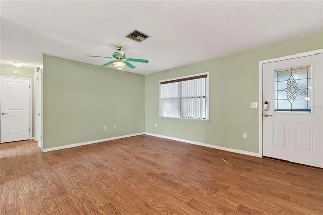 an empty room with wooden floor chandelier fan and windows