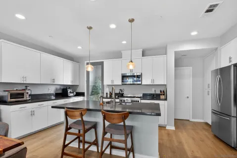 a kitchen with stainless steel appliances kitchen island granite countertop a refrigerator a stove a sink a dining table and chairs with wooden floor