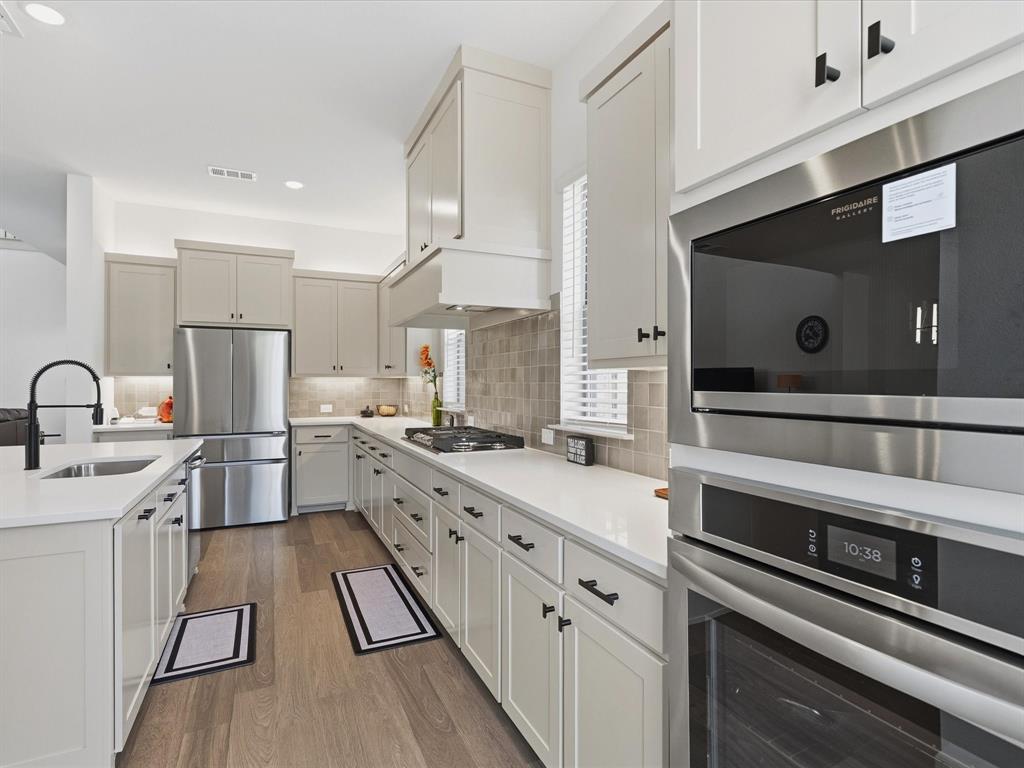 9533 Keep Street Frisco, TX 75035 - Photo 10 of 40 Kitchen featuring wood-finish flooring, light-toned cabinetry with dark hardware, stainless steel appliances, and solid surface countertops