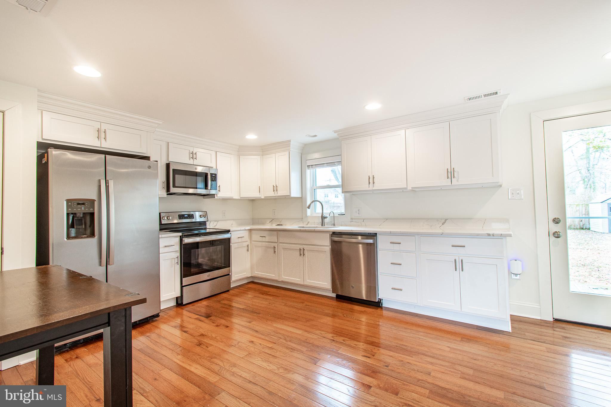 101 Brooks Lane St. Michaels, MD 21663 - Photo 8 of 28 a kitchen with granite countertop a refrigerator oven a sink dishwasher and white cabinets with wooden floor