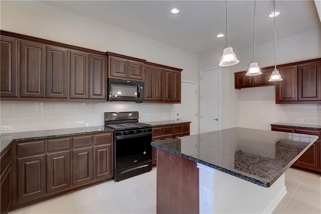 6907 Idea Road Austin, TX 78741 - Photo 11 of 29 Kitchen island with dark cabinets, gas stove, and pendant lights
