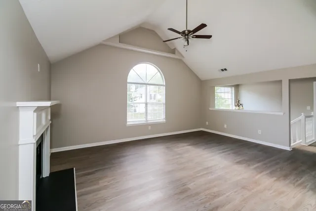 an empty room with wooden floor fan and windows