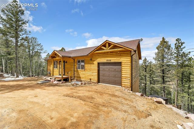 1055 Timber Ridge Road Divide, CO 80814 - Photo 2 of 47 View of front of house featuring faux log siding, a shingled roof, dirt driveway, and a garage