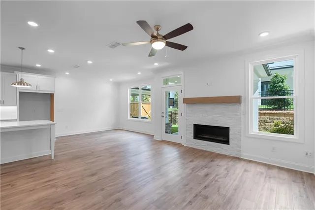 an empty room with windows a fireplace a ceiling fan and wooden floor