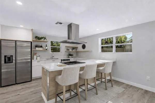 an empty room with wooden floor kitchen view and windows