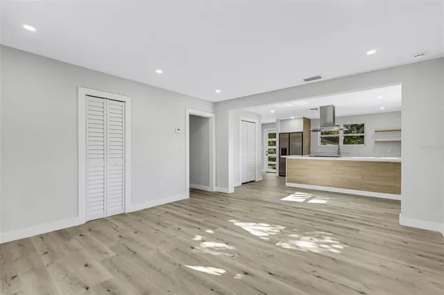 an empty room with wooden floor kitchen view and windows