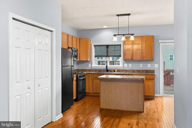 a kitchen with stainless steel appliances granite countertop a refrigerator a sink dishwasher a stove and a dining table with wooden floor